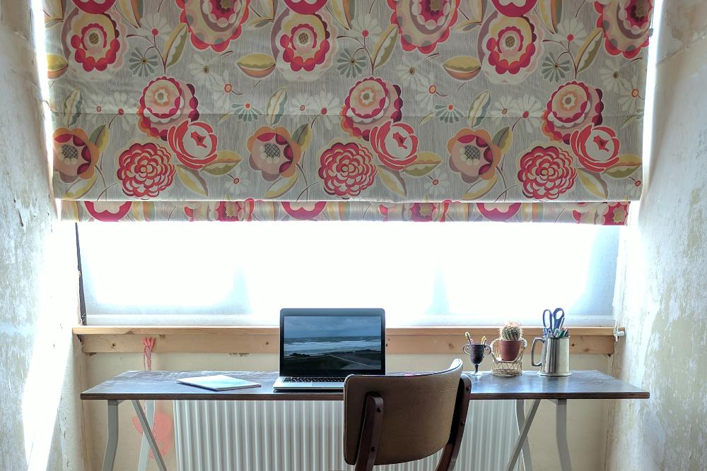 A wood chair in front of a window with a floral shade
